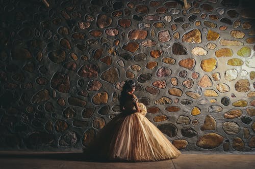 新娘holidng花与背对着镜头站在一堵石墙前的照片 · 免费素材图片