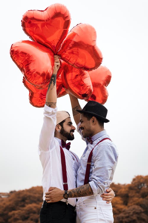 两名男子手持心形气球拥抱 · 免费素材图片