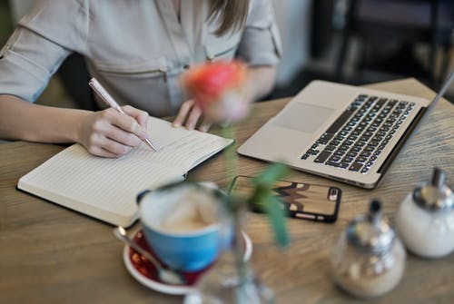 在macbook旁边的笔记本上写的人 · 免费素材图片