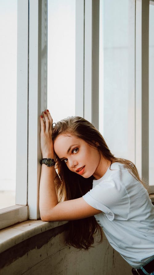 女人穿着白衬衫，倚在玻璃窗口 · 免费素材图片