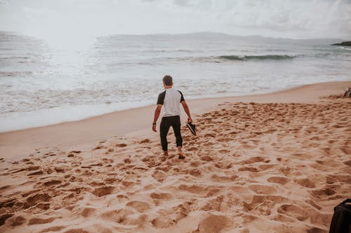 男子手持鞋在岸上 · 免费素材图片