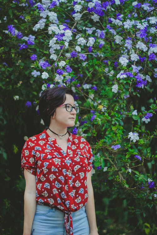 女人穿着红色和蓝色的衬衫站在紫色和白色的花朵旁边 · 免费素材图片