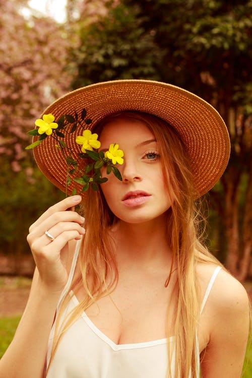 女人戴着草帽，拿着黄色的花朵，在她的脸附近 · 免费素材图片