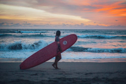 男子携带冲浪板在海边散步 · 免费素材图片