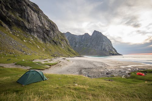 面对海洋的绿色草地上的绿色帐篷 · 免费素材图片