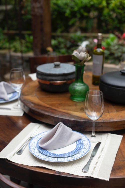 圆形的白色和蓝色陶瓷板和棕色木制的桌子上的空酒杯 · 免费素材图片