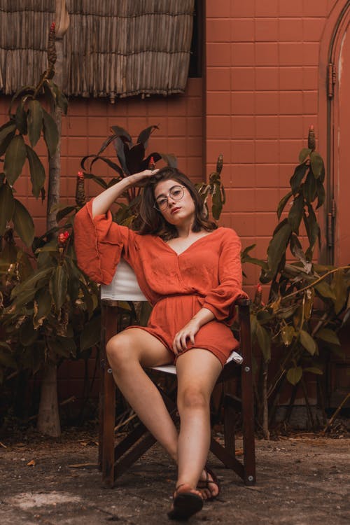 女人穿着橙色暴跌的脖子长袖连身裤坐在椅子上 · 免费素材图片