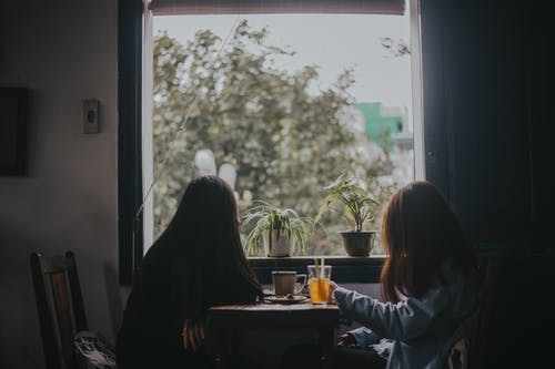 两个女人坐在桌旁，靠近窗户 · 免费素材图片