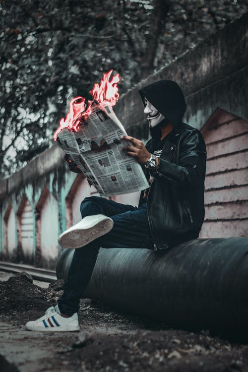 男人戴着面具坐下来，拿着报纸与火 · 免费素材图片
