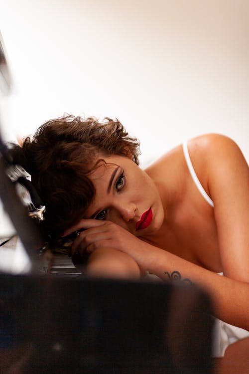 女人穿着白色意大利面条皮带在钢琴旁边 · 免费素材图片