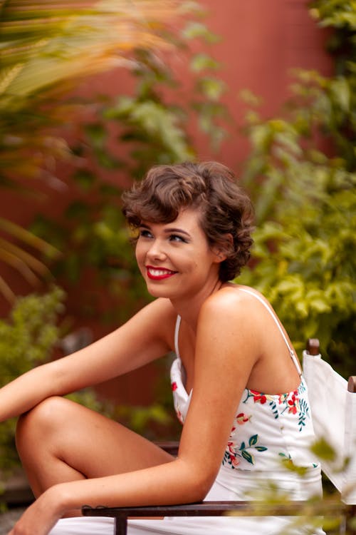 白色无袖连衣裙坐在花园里微笑的女人 · 免费素材图片