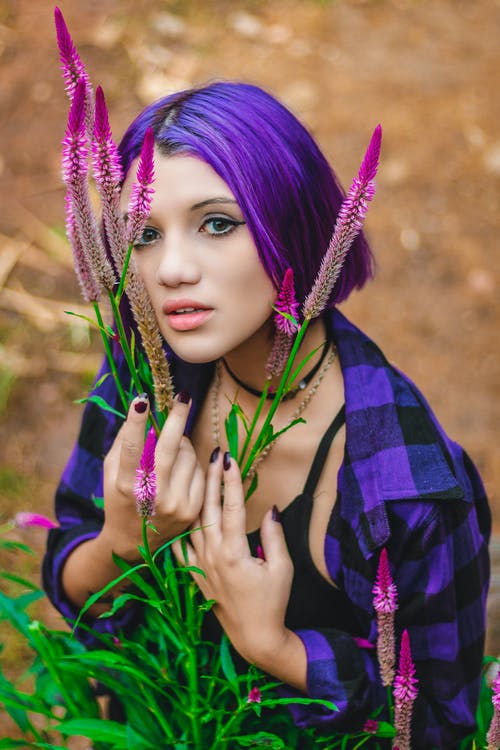 紫色的花朵旁边的紫色和黑色格子领衬衫的紫色头发的女人的照片 · 免费素材图片