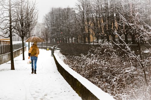 伞在积雪的人行道上行走的女人 · 免费素材图片