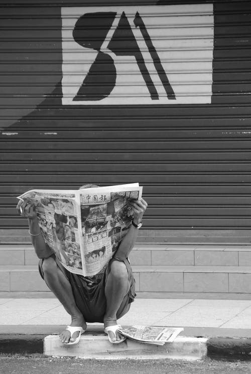 坐在人行道上看报纸的人 · 免费素材图片