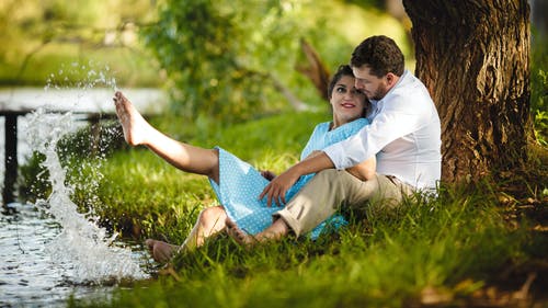 夫妻坐在河边树下的草地上 · 免费素材图片