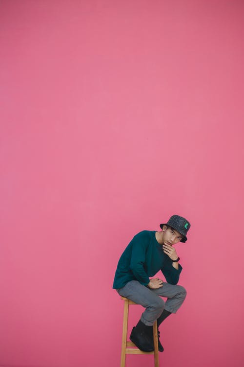 男子坐在木凳上粉红色背景 · 免费素材图片