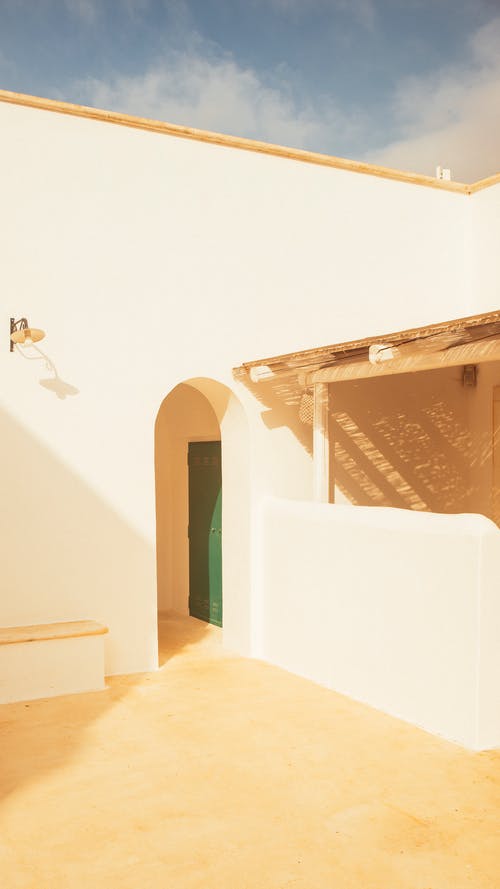 白色混凝土建筑的拱形的入口与壁灯和木制棚在一边 · 免费素材图片