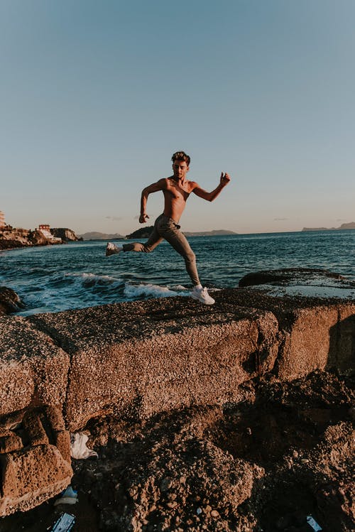 男子跳过岸边的棕色路障 · 免费素材图片