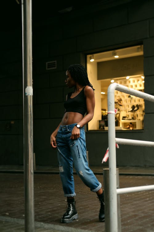 站在商店前面穿着黑色作物顶部抱着她的牛仔裤的女人的照片 · 免费素材图片