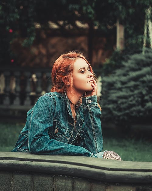 女人靠在绿色的植物附近的灰色混凝土面板上 · 免费素材图片