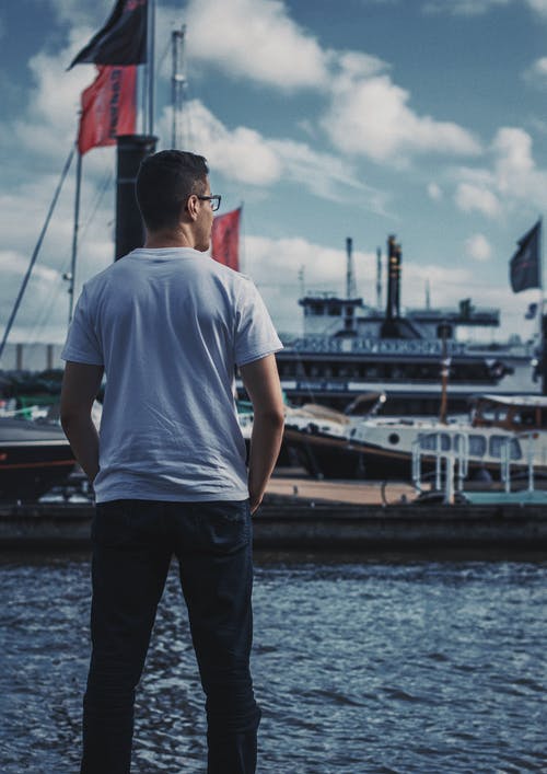 身穿白色圆领衬衫站在海甲板上的男人 · 免费素材图片