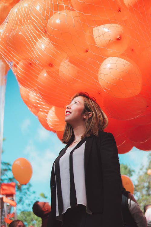 黑色羊毛衫在橙色气球下微笑的女人 · 免费素材图片
