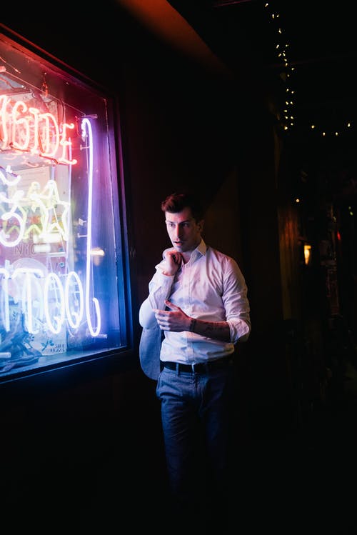 男子身穿白色礼服的衬衫走在led标牌附近 · 免费素材图片