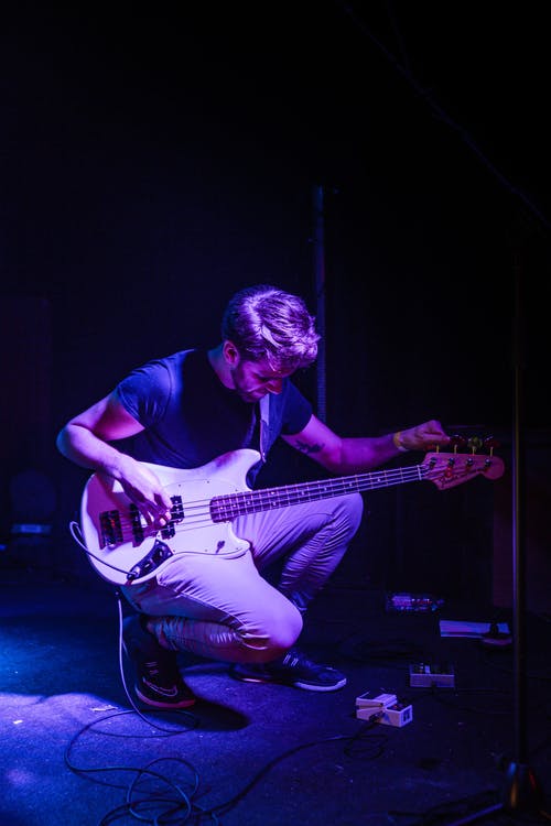男子在舞台上调他的低音吉他 · 免费素材图片