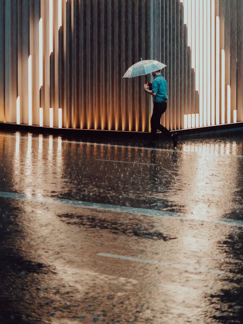 下雨时走在建筑物旁边的男子手持伞的照片 · 免费素材图片