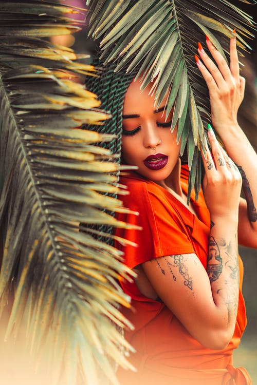 橙色衬衫站在椰子棕榈叶下的女人 · 免费素材图片