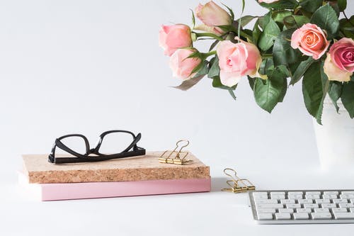玫瑰和键盘旁边的书上的眼镜 · 免费素材图片