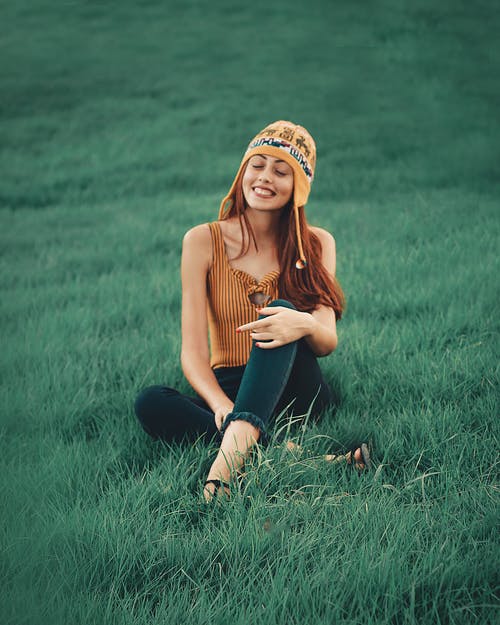 微笑的女士穿着棕色的无袖衬衫，坐在草地上 · 免费素材图片
