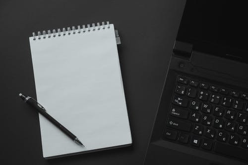 白色steno笔记本旁边的黑色便携式计算机 · 免费素材图片