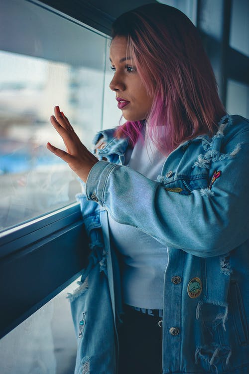 站在窗户旁边的粉红色头发的女人的照片 · 免费素材图片
