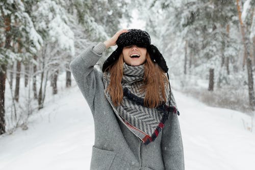 穿着灰色外套的女人拿着帽子，站在积雪覆盖的地面中间 · 免费素材图片