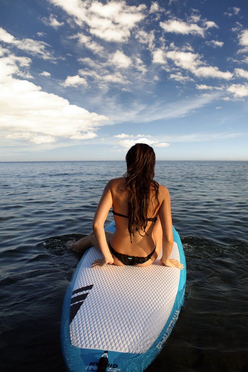 女人坐在白色和蓝色的冲浪板上 · 免费素材图片
