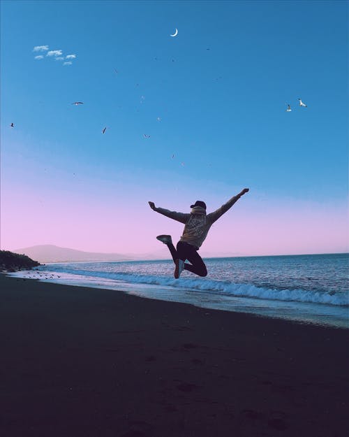 男子在日落海滩上跳跃 · 免费素材图片