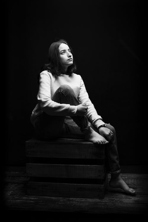 女人坐在木箱上时仰望的灰度照片 · 免费素材图片