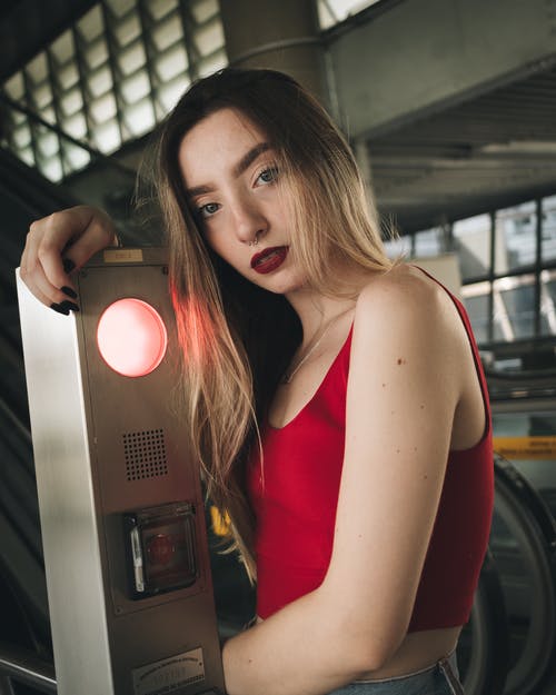 红色背心站着自动扶梯停止按钮机的女人的照片 · 免费素材图片
