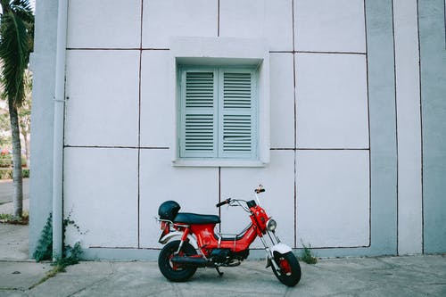 红色摩托车停在白色混凝土建筑旁边 · 免费素材图片