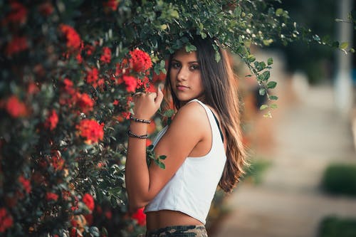站在红色花朵旁边的白色背心的女人 · 免费素材图片