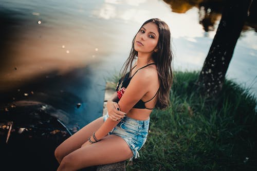 蓝色的短裤和黑色的上衣，坐在水面的石头人行道上的女人的照片 · 免费素材图片