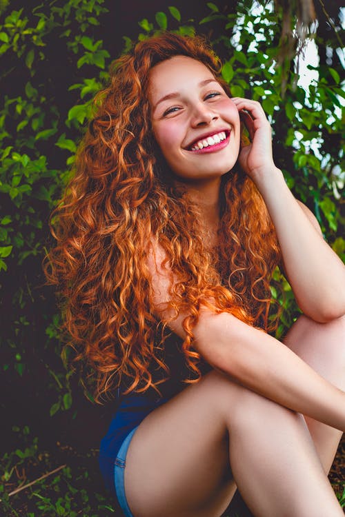 坐在绿叶植物前的微笑妇女 · 免费素材图片