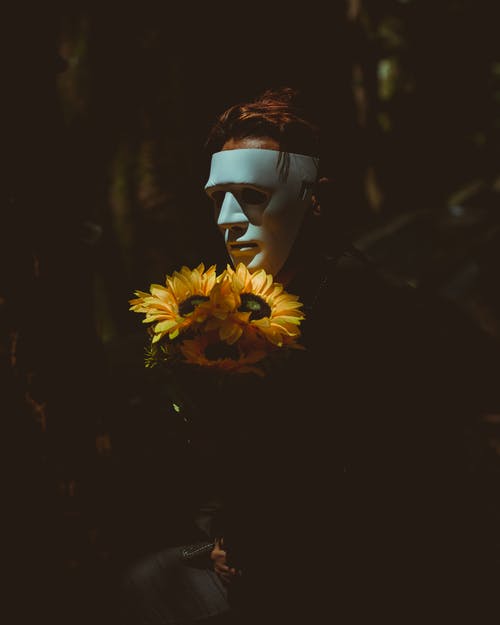 戴着面具拿着向日葵的人 · 免费素材图片