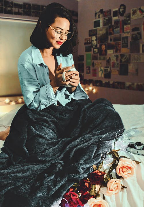 女人坐在床上捧着一杯 · 免费素材图片