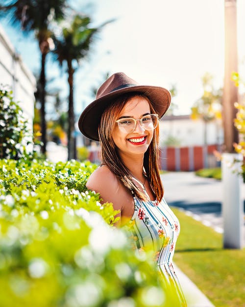 微笑的女人，穿着白色和蓝色条纹的花卉背心和黑色的帽子 · 免费素材图片