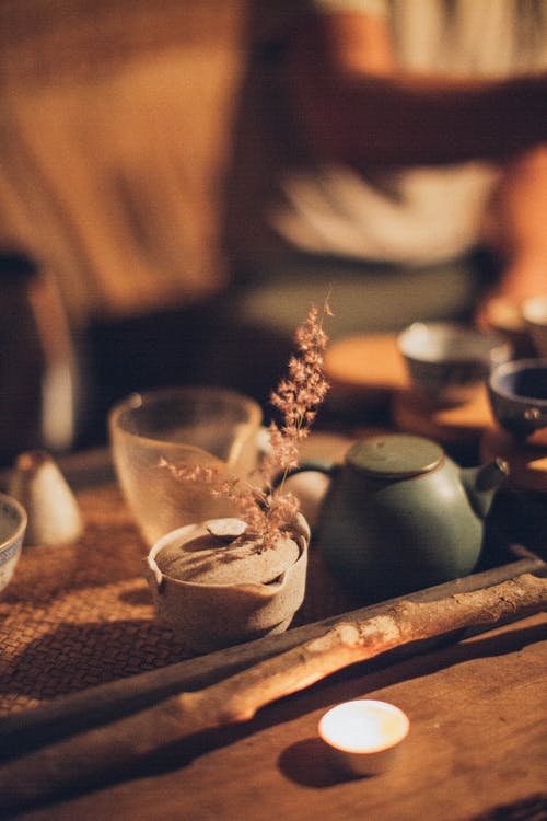 在木棍和陶瓷茶壶旁边的点燃的茶蜡 · 免费素材图片