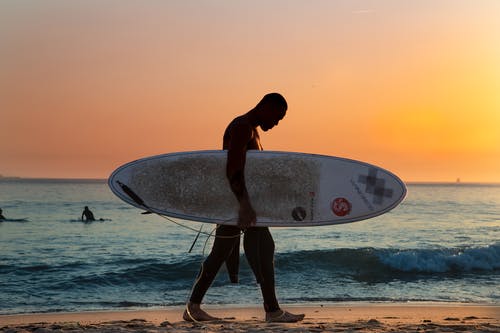 男子携带白色冲浪板上海滩 · 免费素材图片