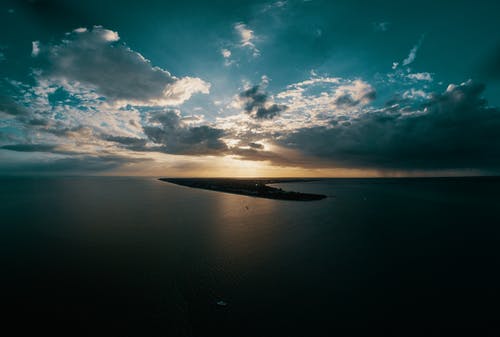 在日落期间的戏剧性云下平静的海面 · 免费素材图片