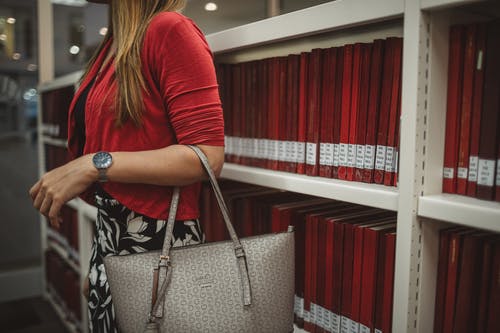 携带灰色手提袋站在红色书柜旁边的女人 · 免费素材图片